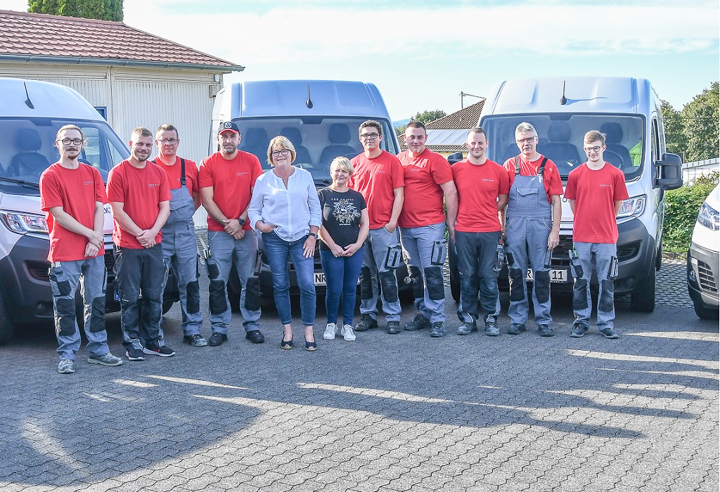 Team Elektro Hoppen GmbH, bestehend aus 11 Mitarbeitenden, darunter 2 Frauen. Das Team steht vor den Firmenautos im Hof des Unternehmens.