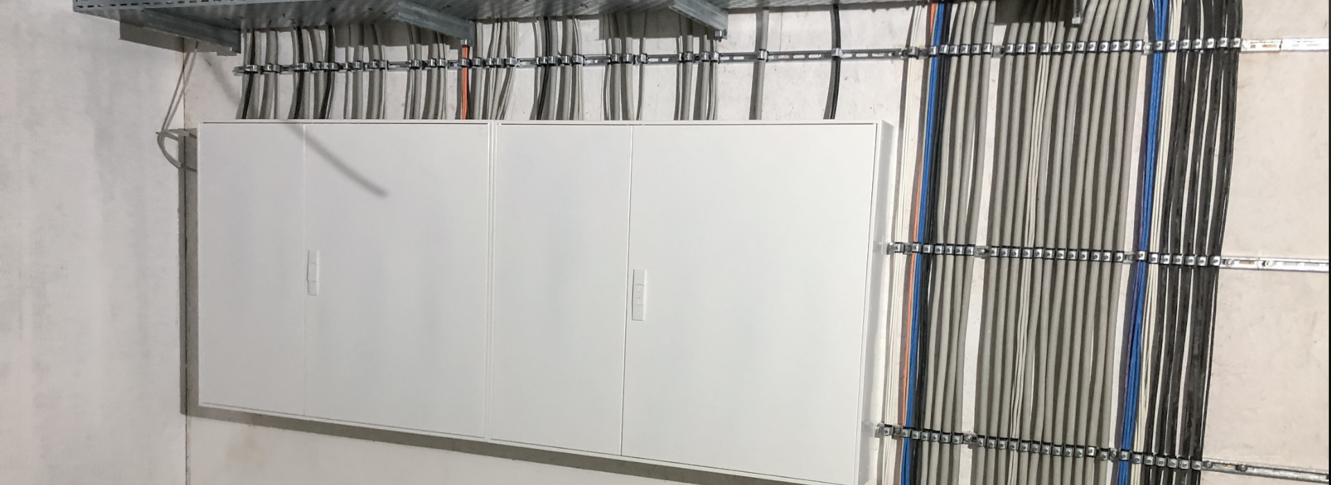 Stromzähler und Baustrom: Das Bild zeigt eine neue Verkabelung in einem renovierten Mehrfamilienhaus, die in einen großen weißen Stromkasten führt.