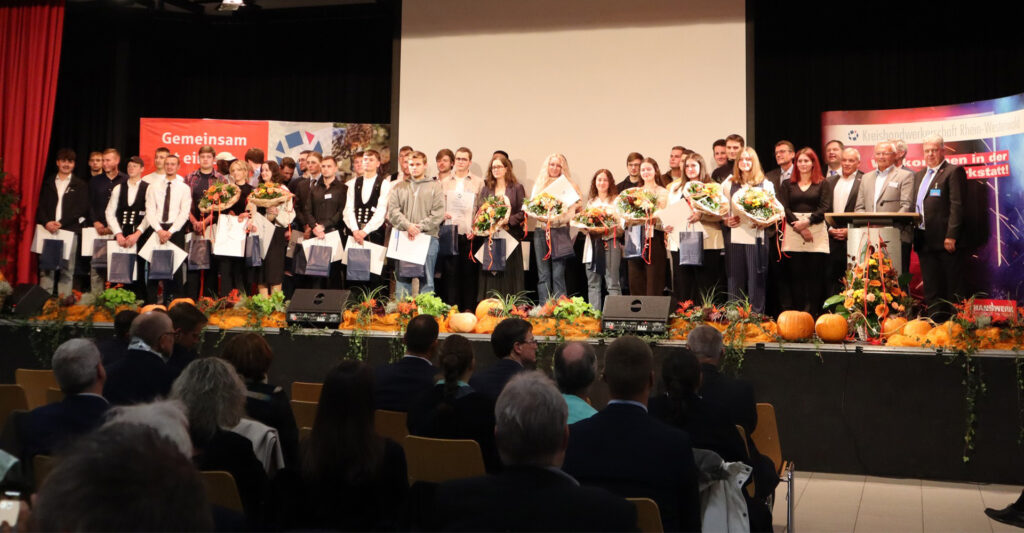 Gruppenfotos der besten Azubis des Jahrgangs auf der Bühne der Wiedparkhalle. Die jungen Frauen und Männer halten Blumensträuße und Urkunden in den Händen.