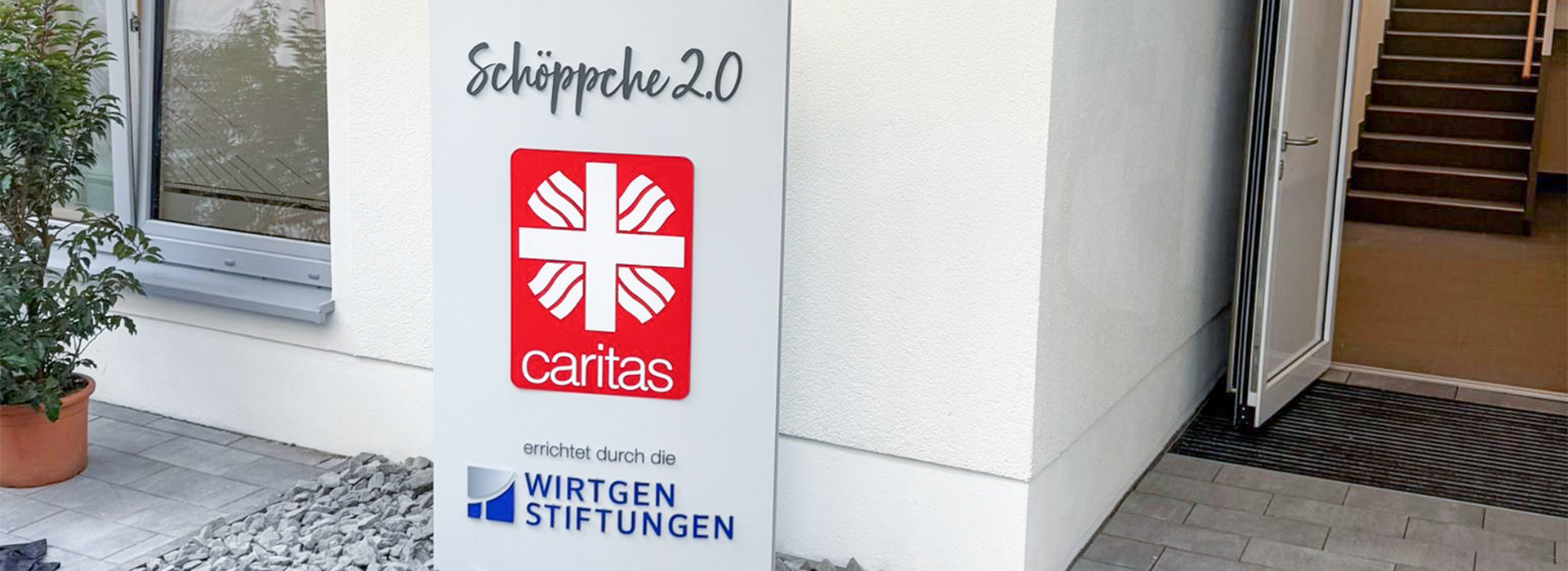 Schild vor dem Eingang: "Schöppche 2.0" mit den Logos der Caritas und der Wirtgen Stiftungen